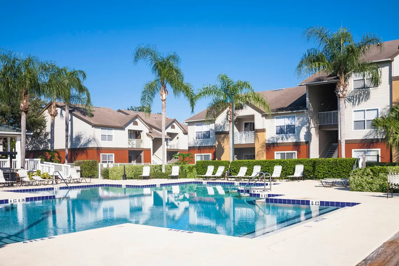 Swimming pool at a condominium complex. Palm trees, chaise lounge, clear sky.