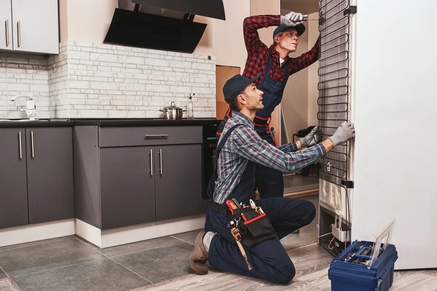 Two mechanics checking refrigerator with screwdriver. 