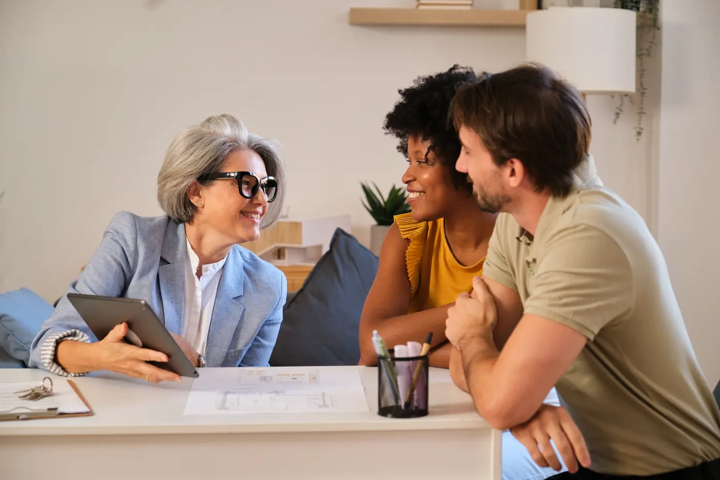 A property manager presenting investment information on a tablet to a young couple during a home consultation.