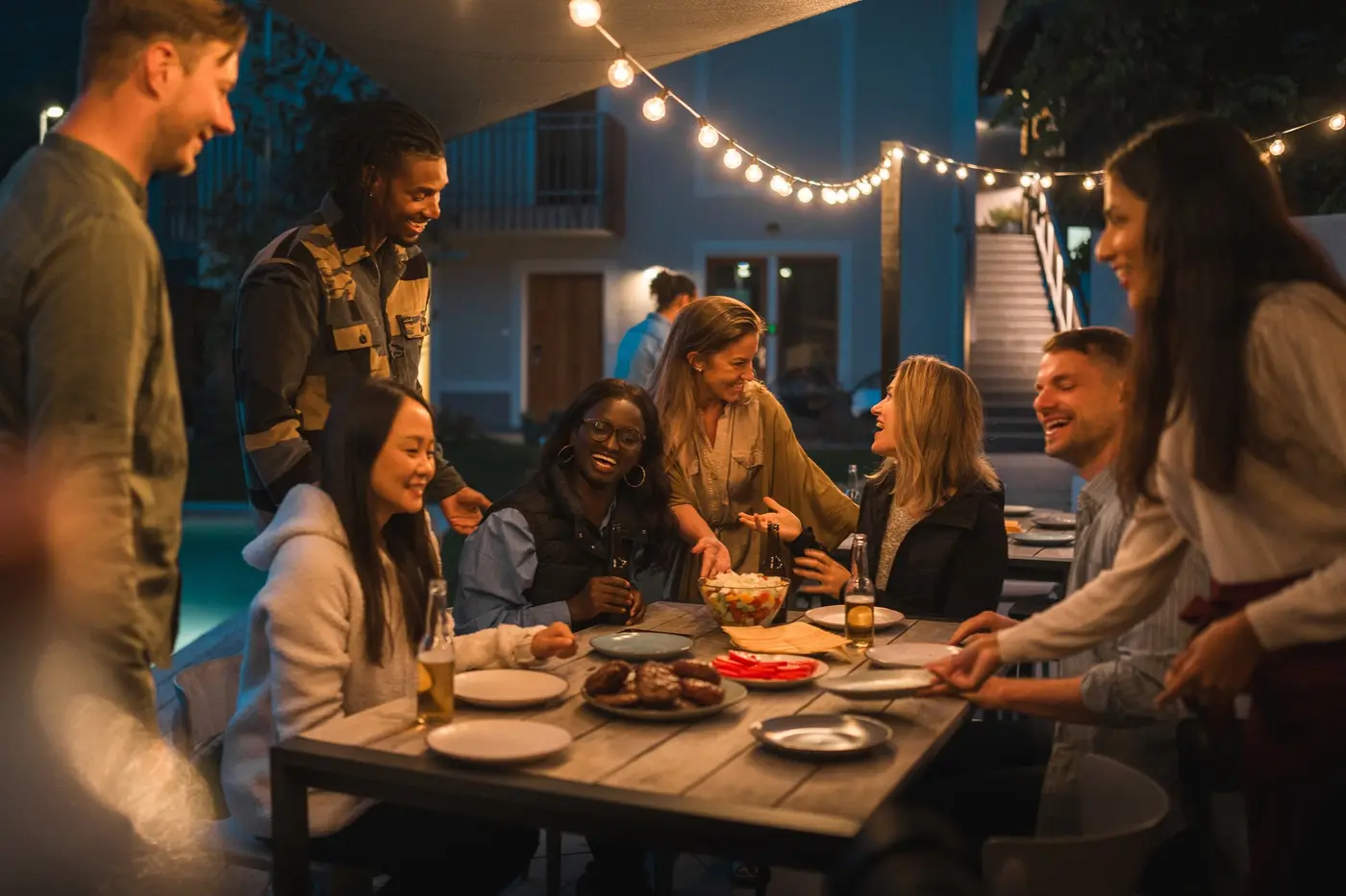 Group of diverse male and female friends gather around a table for an evening meal.
