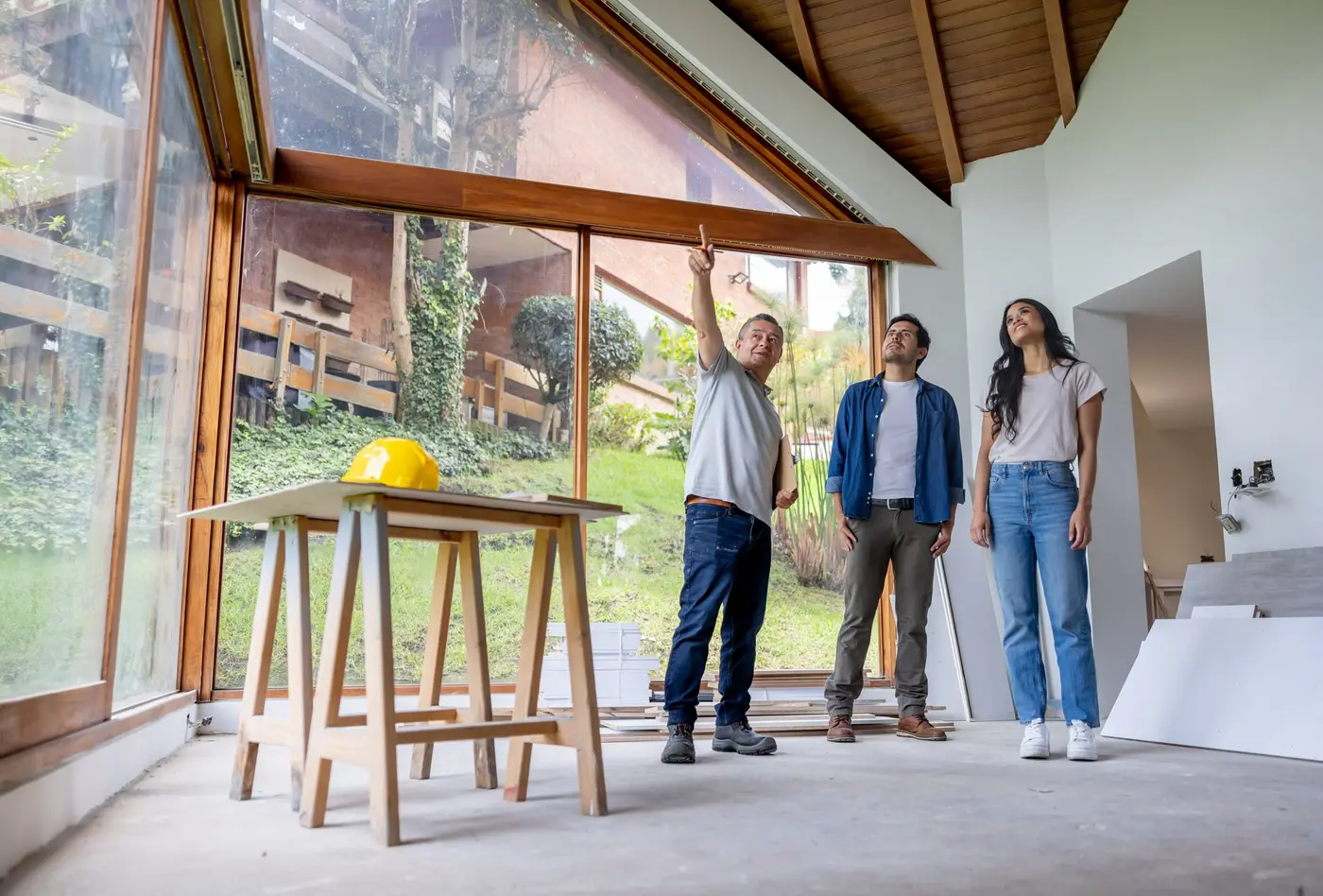 A building contractor and homeowners stand in an unfinished house, discussing renovation plans.
