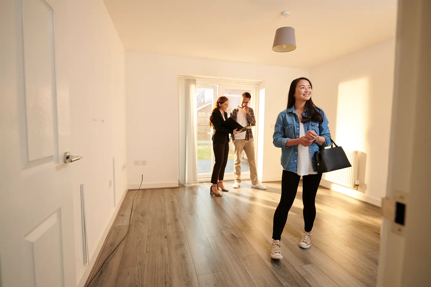 A potential tenant standing in an empty room of a rental home with two others engaged in conversation. 
