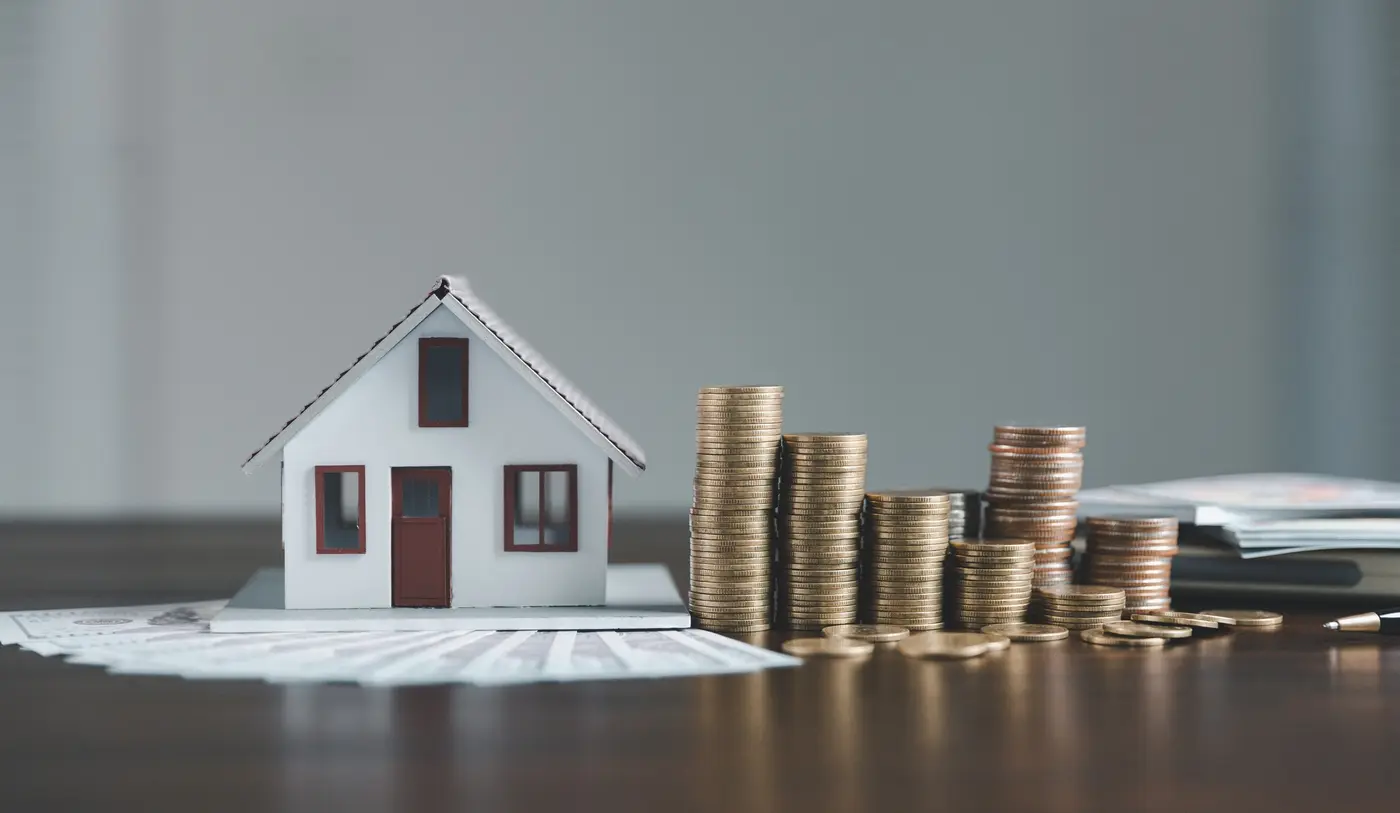 A small house model next to a pile of coins on a wooden table, symbolizing investment in real estate.