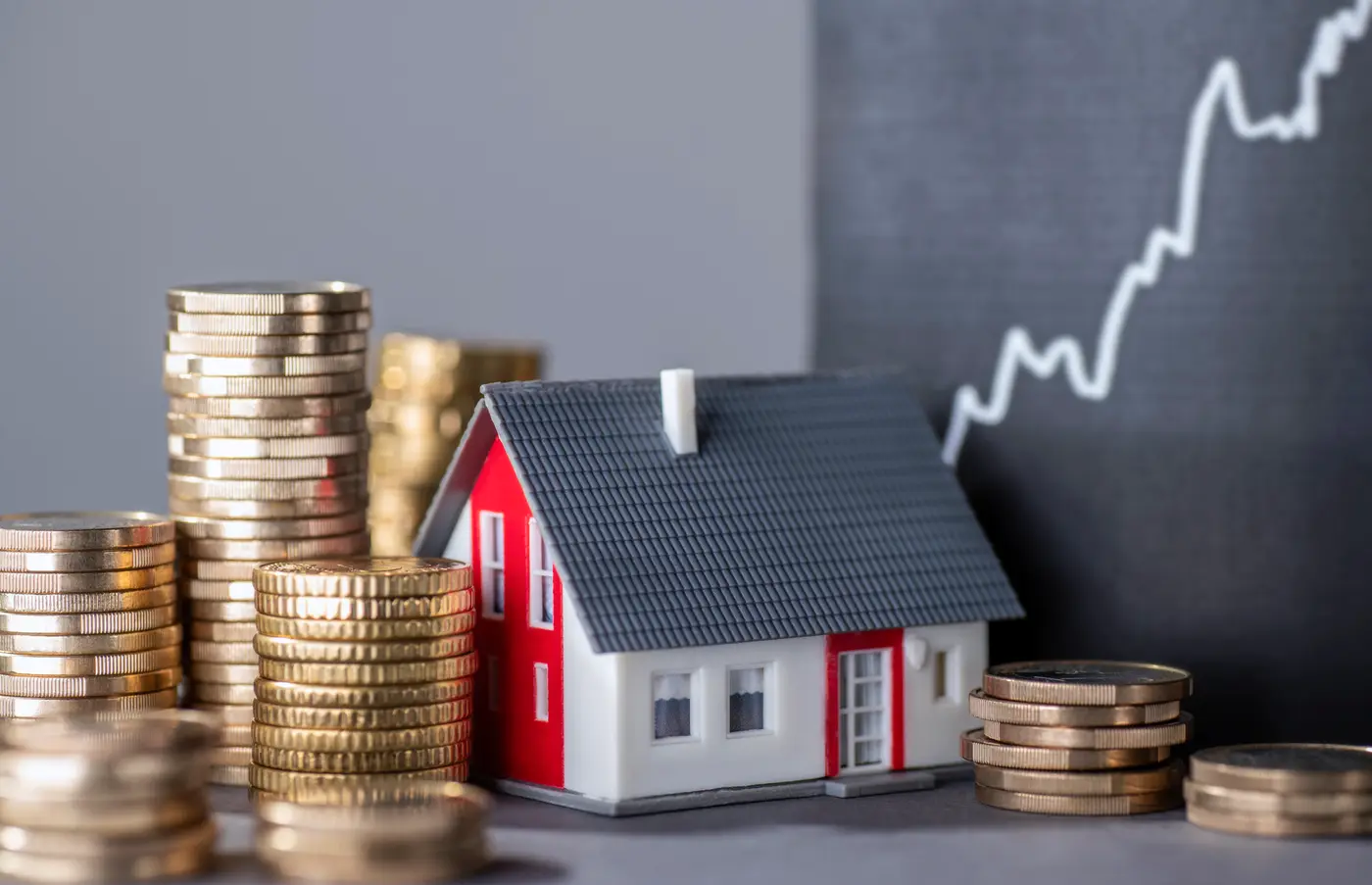 Small model home among stacks of coins and minimalist growth chart behind off to the side.
