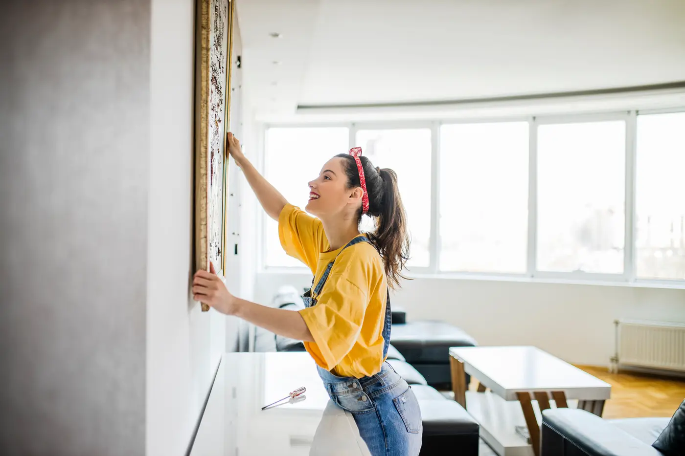 A woman happily hanging a picture on the wall of her rental home.