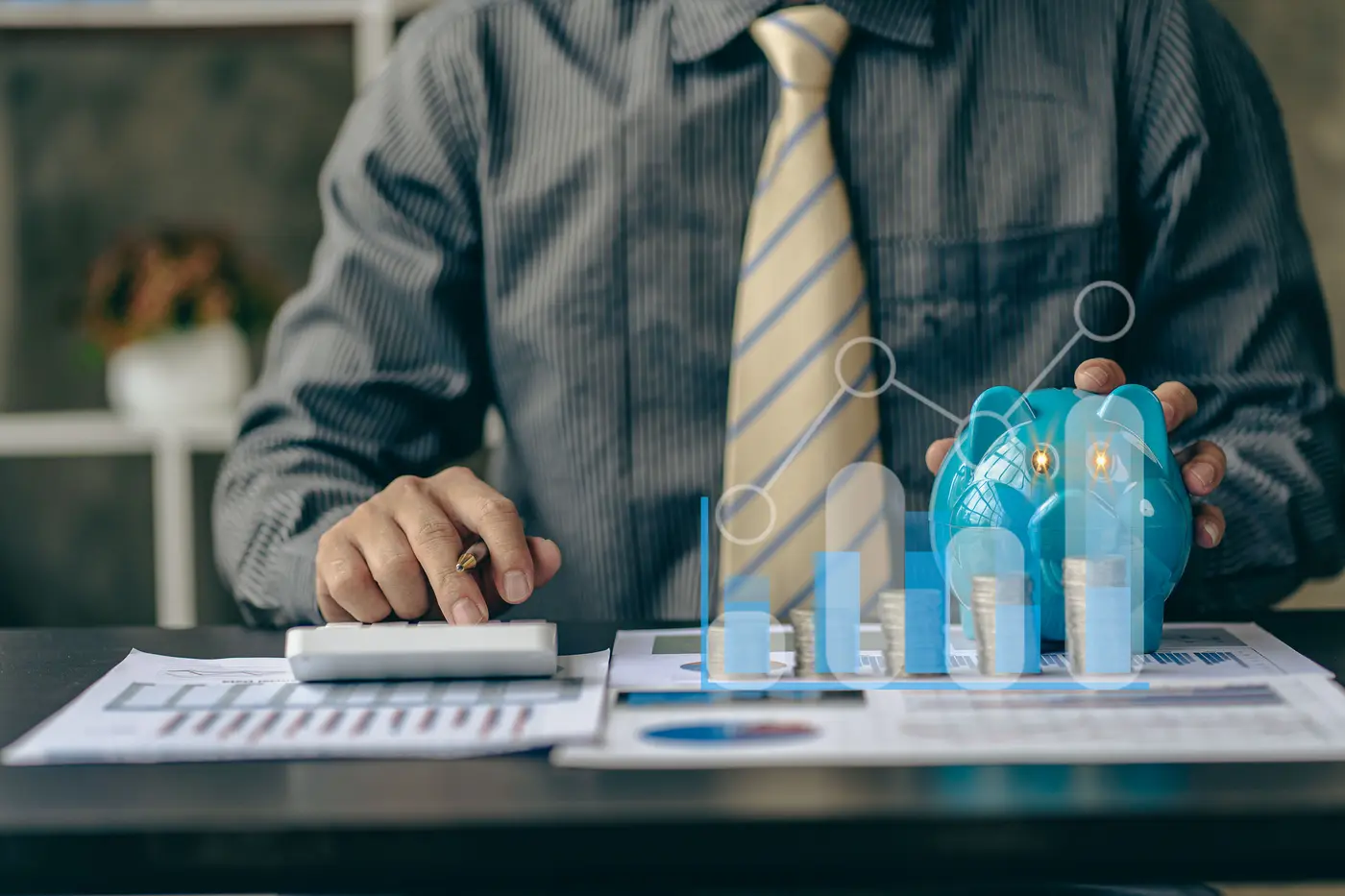 Businessman calculating finances with piles of coins on the side with piggy banks, financial graph, savings concept.