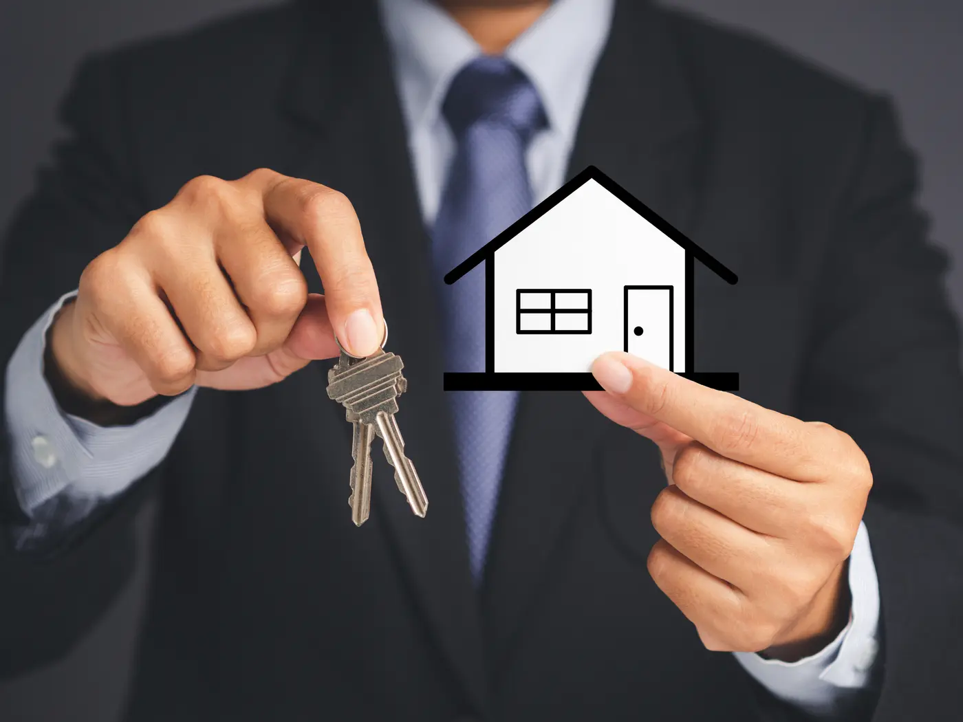 Business and real estate concept. A businessman's hands holding a bunch of two keys and mini paper house over a gray background. Property insurance and security.