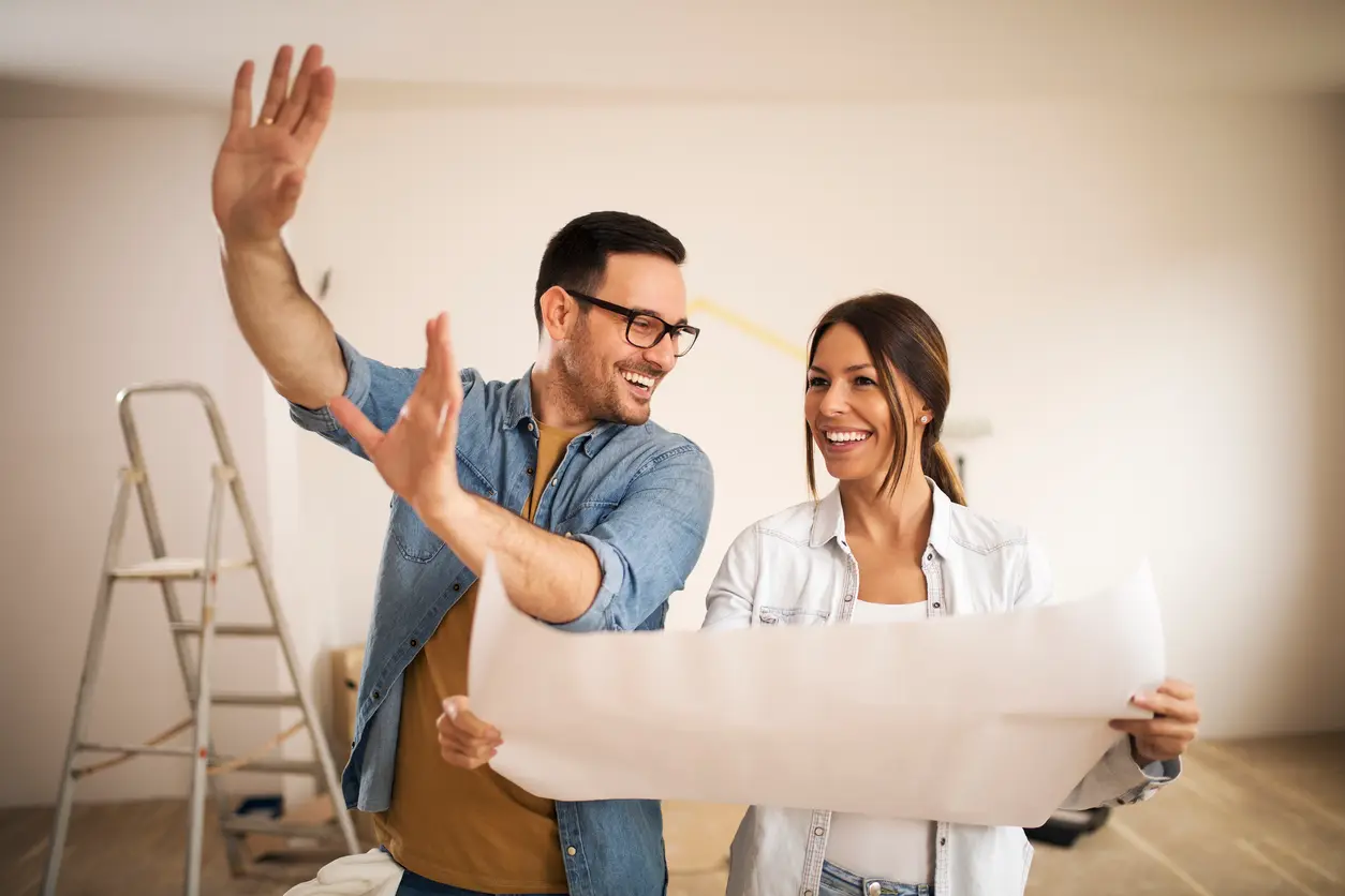 Young couple standing in their apartment while woman holding blueprint and man showing her new ideas.